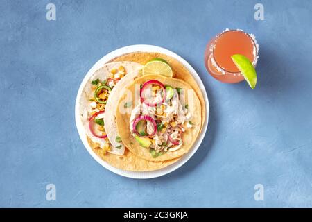 Mexikanische Tacos, Tortillas mit Hühnerfleisch, Avocado, Mais und Zwiebeln, mit dem Paloma-Cocktail, von oben geschossen Stockfoto