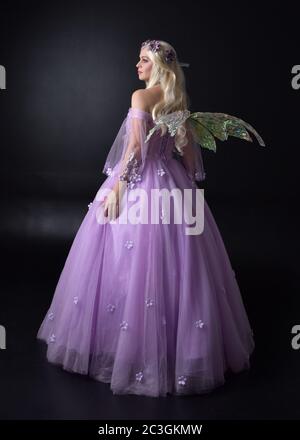 Portrait einer schönen blonden Fee trägt lila Fantasy-Kleid mit Flügeln. In voller Länge stehende Pose, isoliert vor einem Studio-Hintergrund. Stockfoto