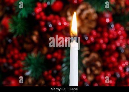 Weiße Kerze und weihnachtlicher Hintergrund mit roten Beeren, Zapfen und Tannenzweigen. Festliche Einrichtung Stockfoto