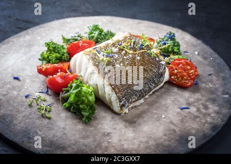 Gourmet-gebratenes europäisches Skrei-Kabeljau-Fischfilet mit Kalette und Tomaten als Nahaufnahme auf einem modernen Design-Teller Stockfoto