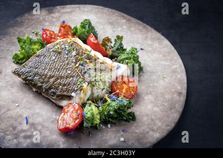 Gourmet-gebratenes europäisches Skrei-Kabeljau-Fischfilet mit Kalette und Tomaten als Nahaufnahme auf einem modernen Design-Teller mit Kopierplatz rechts Stockfoto