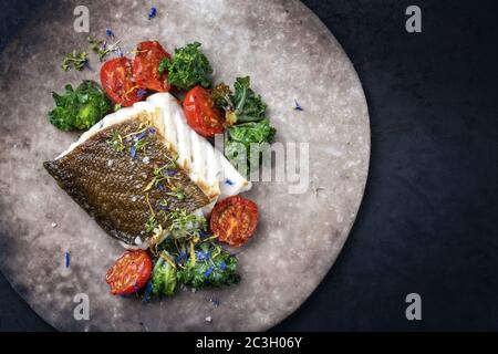 Gourmet-gebratenes europäisches Skrei-Kabeljau-Fischfilet mit Kalette und Tomaten als Draufsicht auf einem modernen Design-Teller mit Kopierplatz rechts Stockfoto