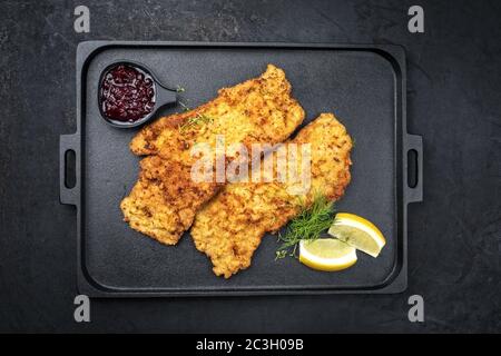 Traditionelle frittierte Wiener Schnitzel aus Kalbtopside mit Cranberry-Marmelade und Zitronenscheiben als Draufsicht auf einem schwarzen Mod angeboten Stockfoto