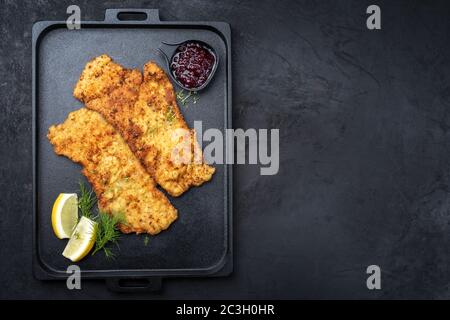 Traditionelle frittierte Wiener Schnitzel aus Kalbtopside mit Cranberry-Marmelade und Zitronenscheiben als Draufsicht auf einem schwarzen Mod angeboten Stockfoto