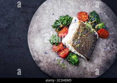 Gourmet-gebratenes europäisches Skrei-Kabeljau-Fischfilet mit Kalette und Tomaten als Draufsicht auf einem modernen Design-Teller mit Kopieplatz links Stockfoto