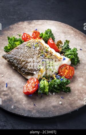 Gourmet-gebratenes europäisches Skrei-Kabeljau-Fischfilet mit Kalette und Tomaten als Nahaufnahme auf einem modernen Design-Teller mit Kopierfläche Stockfoto