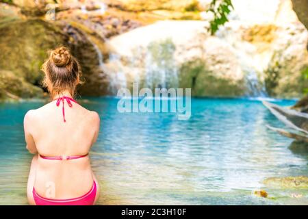 Rückansicht einer jungen Frau, die am smaragdblauen See sitzt Stockfoto