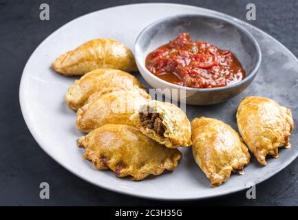 Traditionelle südamerikanische Empanada de Carne mit einem Chili-Dip als Nahaufnahme auf einem modernen Design-Teller angeboten Stockfoto