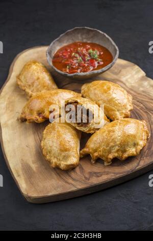 Traditionelle südamerikanische Empanada de Carne mit einem Chili-Dip als Nahaufnahme auf einem rustikalen Holzbrett angeboten Stockfoto