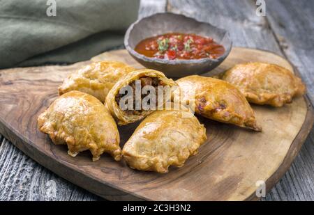 Traditionelle südamerikanische Empanada de Carne mit einem Chili-Dip als Nahaufnahme auf einem rustikalen Holzbrett angeboten Stockfoto