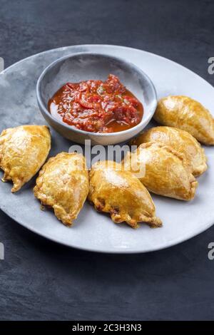 Traditionelle südamerikanische Empanada de Carne mit einem Chili-Dip als Nahaufnahme auf einem modernen Design-Teller angeboten Stockfoto