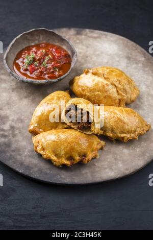 Traditionelle südamerikanische Empanada de Carne mit einem Chili-Dip als Nahaufnahme auf einem rustikalen, modernen Design-Teller angeboten Stockfoto