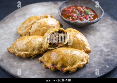 Traditionelle südamerikanische Empanada de Carne mit einem Chili-Dip als Nahaufnahme auf einem rustikalen, modernen Design-Teller angeboten Stockfoto