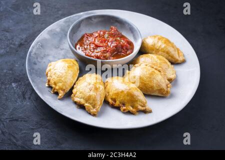Traditionelle südamerikanische Empanada de Carne mit einem Chili-Dip als Nahaufnahme auf einem modernen Design-Teller angeboten Stockfoto