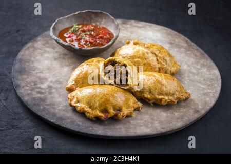 Traditionelle südamerikanische Empanada de Carne mit einem Chili-Dip als Nahaufnahme auf einem rustikalen, modernen Design-Teller angeboten Stockfoto