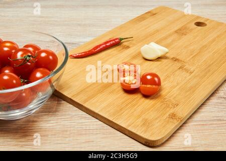 Stillleben in der Küche mit Kirschtomaten, Chili und Knoblauchscheiben auf einem Schneidebrett Stockfoto