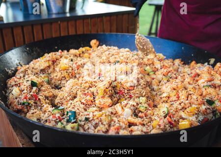 Große schwarze Pfanne voll mit Essen. Mischung aus Reis, Gemüse und Meeresfrüchten - wahrscheinlich Paella. Feier, Party, Geburtstag oder Hochzeit Konzept. Stockfoto