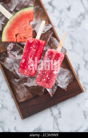 Das Servieren einer Sommerparty. Rot gefrorenes Sorbet mit dem Geschmack von Wassermelone liegt auf großen Eisstücken mit Stücken von reifen Wassermelone Stockfoto