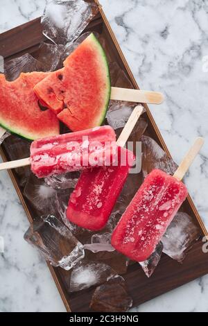 Das Servieren einer Sommerparty. Rot gefrorenes Sorbet mit dem Geschmack von Wassermelone liegt auf großen Eisstücken mit Stücken von reifen Wassermelone Stockfoto