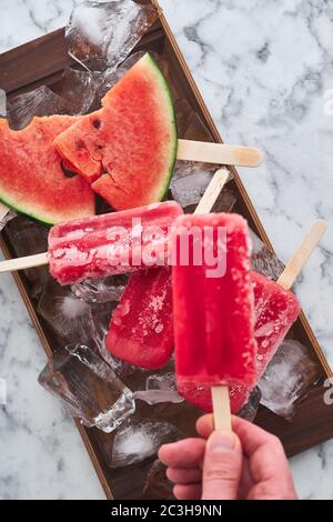 Das Servieren einer Sommerparty. Rot gefrorenes Sorbet mit dem Geschmack von Wassermelone liegt auf großen Eisstücken mit Stücken von reifen Wassermelone Stockfoto