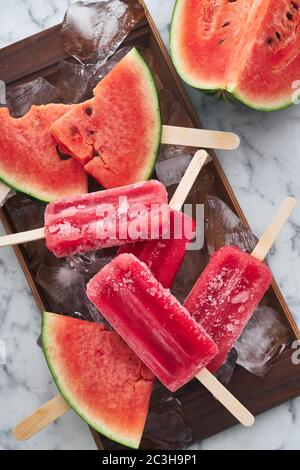 Das Servieren einer Sommerparty. Rot gefrorenes Sorbet mit dem Geschmack von Wassermelone liegt auf großen Eisstücken mit Stücken von reifen Wassermelone Stockfoto