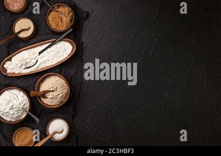 Verschiedene Arten von Mehl in Holzschalen auf schwarzem Tisch, Draufsicht Stockfoto