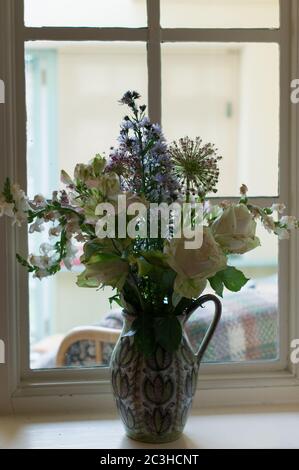 Ein Bündel von blassrosa, weißen und malvenfarbenen Blüten in einem Denby-Krug auf einer Fensterbank Stockfoto