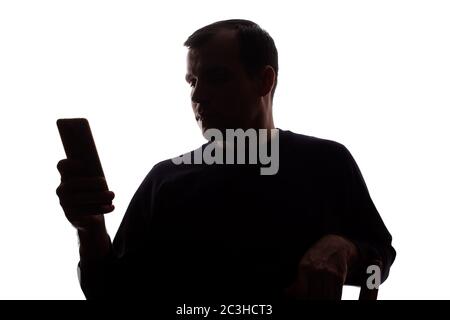 Der junge Mann sitzt auf einem Stuhl mit einem Handy in der Hand - Silhouette, Internet-Konzept, Kommunikation Stockfoto