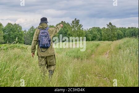 Aktiver Mann im Mückenanzug mit Rucksack beim Wandern auf einer Wiese. Sibirien, Russland. Alleinreisen, Lifestyle, inländisches Tourismuskonzept Stockfoto