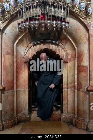 Ein griechisch-orthodoxer Geistlicher kommt aus der Rotunde Edicule oder Anastasia, die die Engelskapelle enthält, eine Vorkammer, die zum Grab Jesu Christi führt, in der Kirche des Heiligen Grabes in der Altstadt von Jerusalem, Israel. Stockfoto