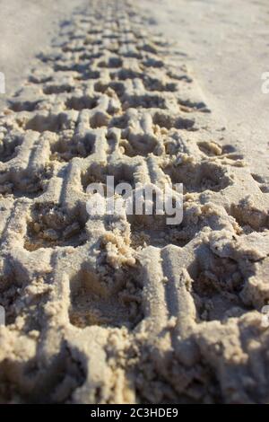 Fußabdruck im Sand von einem Autoreifen oder quadro-Zyklus bei Sonnenaufgang auf einem Hintergrund von blauem Himmel und Meer, Horizont Strand Dämmerung Stockfoto