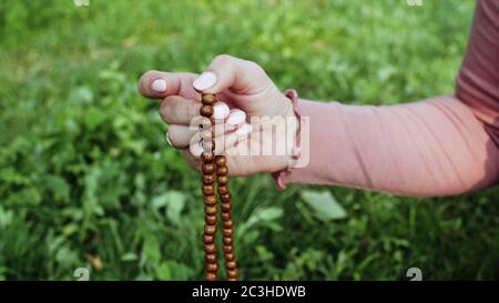 Frau beleuchtet Hand Nahaufnahme zählt Rosenkranz - Malas Stränge von Edelsteinen Perlen für Zählung während Mantra Meditationen verwendet. Mädchen sitzt auf Sommer Natur. Stockfoto