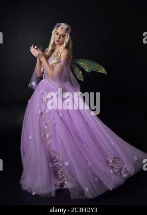 Portrait einer schönen blonden Fee trägt lila Fantasy-Kleid mit Flügeln. In voller Länge stehende Pose, isoliert vor einem Studio-Hintergrund. Stockfoto