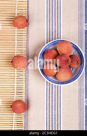 Lycheesin eine traditionelle chiesische blau-weiße Schale mit Bambusmatte und gestreifter Tischdecke Stockfoto