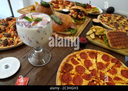 Pizza, Burger und Erdbeereis auf dem Holztisch Stockfoto