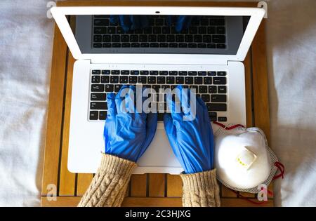 Ein High-Angle-Schuss einer weiblichen Hände mit blauen Handschuhen auf Laptop mit Sauerstoffmaske daneben tippen Stockfoto