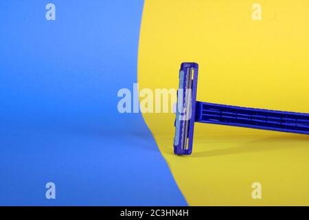 Nahaufnahme eines blauen Rasierers mit zwei Klingen auf gelb-blauem Hintergrund Stockfoto