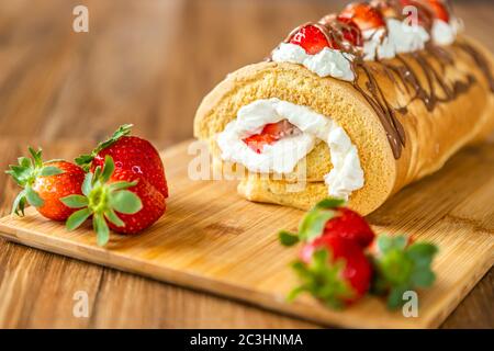 Biskuitroulade mit Mascarpone-Sahne, Erdbeeren und Schokolade, auf einem Holzbrett ausgelegt. Stockfoto