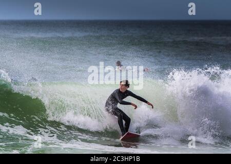Spektakuläre Action als männlicher Surfer auf einer Welle im Fistral in Newquay in Cornwall reitet. Stockfoto