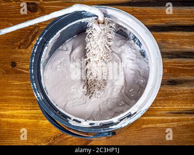Eine kompakte Walzenbürste auf der dicken Oberfläche einer offenen Dose Emulsionsfarbe, auf einer Kiefernoberfläche. Stockfoto