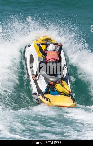 Spektakuläre Action als RNLI Rettungsschwimmer fährt einen Jetski über eine Welle bei Fistral in Newquay in Cornwall. Stockfoto