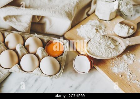 Backgeräte und Backzutaten mit Eiern, Weizenmehl, Eigelb für Gebäck. Kuchen, Pasta oder Teig Rezept Zutaten. Draufsicht auf dem Tisch Stockfoto