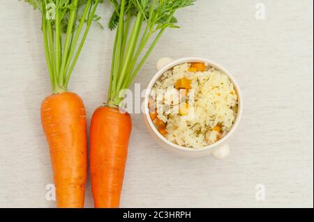 Vegetarische / vegane Küche - Rohe Karotten mit Blättern und eine Schüssel gekochten Reis mit Karotten. Isoliert auf weißem Hintergrund. Speicherplatz kopieren. Draufsicht. Stockfoto