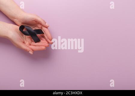 Schwarzes Bewusstseinsband in Handflächen auf rosa Hintergrund Stockfoto