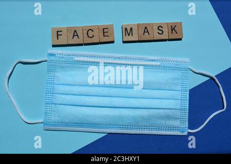 Gesichtsmaske, Wort und eine Einweg-3-lagige nicht-chirurgische Gesichtsmaske mit elastischen Ohrbügel isoliert auf blauem Hintergrund Stockfoto