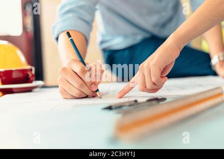 Ingenieure halten einen Stift, der auf ein Gebäude zeigt, und zeichnen den Bauplan als Leitfaden für Bauherren mit Details Stockfoto