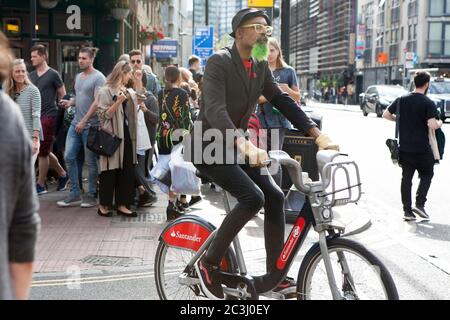 London, Großbritannien - 17. Juli 2019, EIN Hipster mit grünem Bart, in einer engen Jacke und schwarzen Jeans auf einem Fahrrad, durchquert die Menge auf der bricklane Street Stockfoto