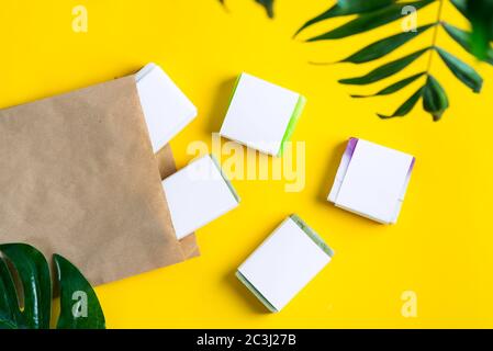 Bunte handgemachte Kräuter-Naturseife mit Mockup Papier Etikett und papercraft umweltfreundliche Tasche auf einem gelben Hintergrund mit grünen troical Blätter. Eg Stockfoto
