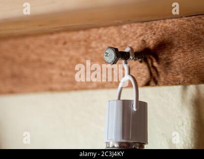 Eine große Schraube an einem braunen Holzbrett und einem hängenden Objekt und cremefarbenen Wand genagelt Stockfoto