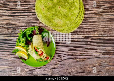 Wickeln Sie mit gegrilltem Huhn und Gemüse auf Spinat grünen Tortillas auf Holztisch. Stockfoto